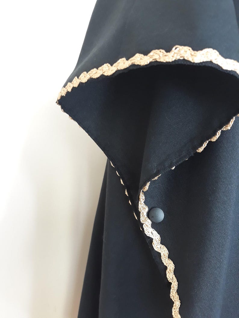 A close-up of a black linen garment with gold trim along the collar and a single gray button closure.