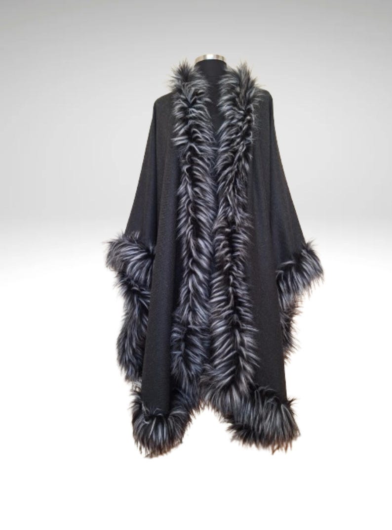 May include: A dark grey cape with faux fur trim. The cape has a wide collar and cuffs trimmed with long, grey and white faux fur. The cape is displayed on a mannequin against a plain background.