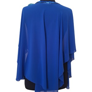 May include: Royal blue cape shawl with a flowing design. The shawl has a sequined neckline and a decorative embellishment on the shoulder. The fabric drapes elegantly, creating a sophisticated look. This accessory is suitable for formal events.