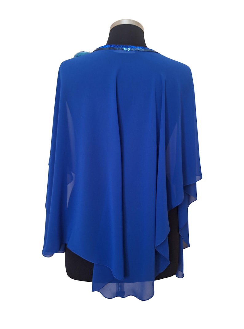 May include: Royal blue cape shawl with a flowing design. The shawl has a sequined neckline and a decorative embellishment on the shoulder. The fabric drapes elegantly, creating a sophisticated look. This accessory is suitable for formal events.