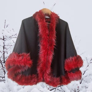 “Elegant black alpaca half cape with luxurious red vegan fur trim, photographed in a natural lighting. The rich contrast of red and black creates a striking, festive look perfect for cold days. Designed by HandmadeByNadya — timeless elegance in motion.”