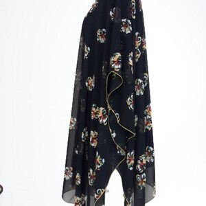 Puede incluir: Un kimono negro de gasa con estampado floral en tonos amarillos, rojos y verdes. El kimono tiene una silueta larga y fluida y un dobladillo ligeramente asim&eacute;trico.