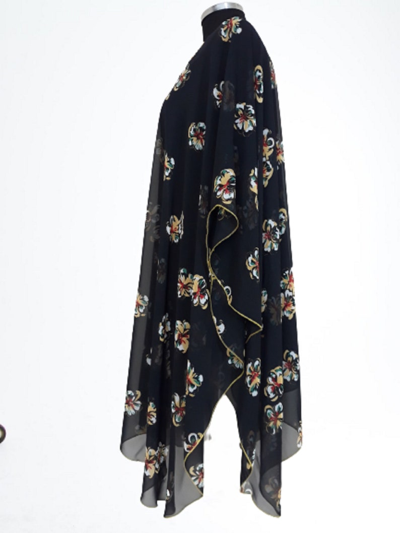 Puede incluir: Un kimono negro de gasa con estampado floral en tonos amarillos, rojos y verdes. El kimono tiene una silueta larga y fluida y un dobladillo ligeramente asim&eacute;trico.
