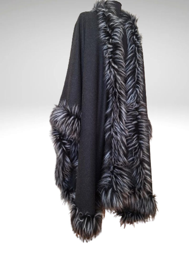 May include: A dark grey cape with faux fur trim. The cape has a high collar and is trimmed with black, white, and grey faux fur along the edges and around the sleeves. The cape is displayed against a white background.