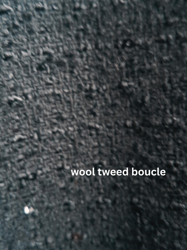 Close-up view of a black wool tweed boucle fabric. The texture is thick and nubby with a slightly irregular surface. The image includes the text 'wool tweed boucle' in white sans-serif font.