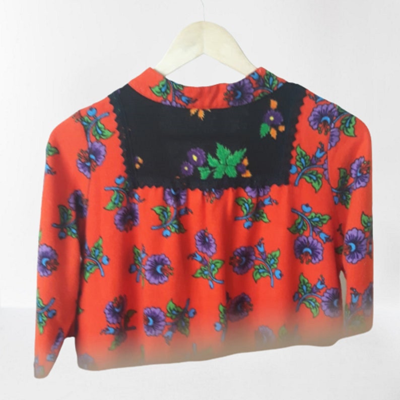 A red dress with a black embroidered collar and a floral print. The flowers are purple, blue, and green.