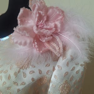 May include: A light green dress with a pink flower and white feathers on the shoulder.