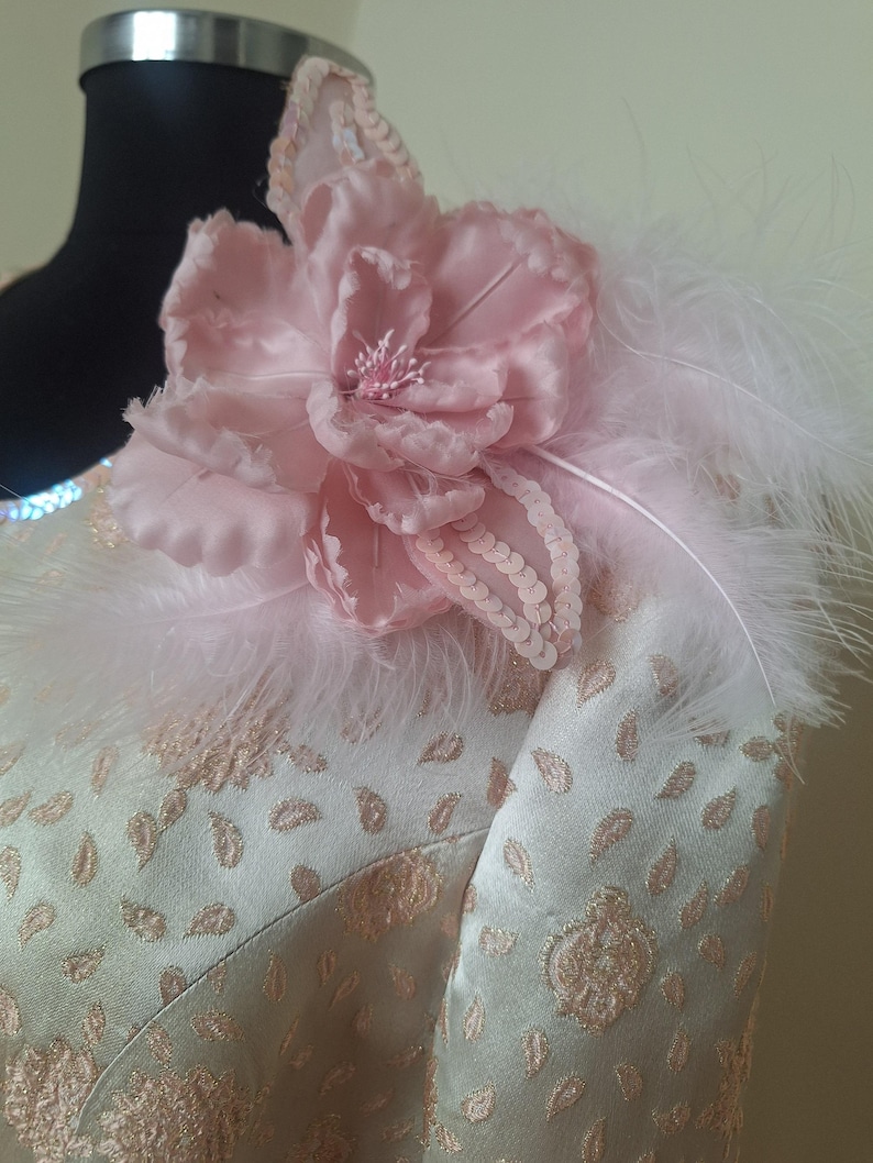 May include: A light green dress with a pink flower and white feathers on the shoulder.
