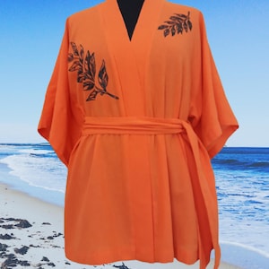 Puede incluir: Batista de kimono naranja con estampado de hojas negras. La bata tiene un cintur&oacute;n de atar y mangas anchas.