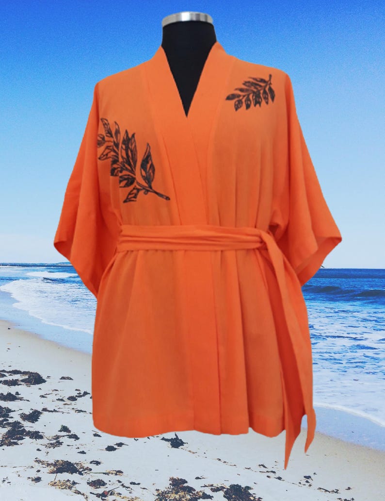 Puede incluir: Batista de kimono naranja con estampado de hojas negras. La bata tiene un cintur&oacute;n de atar y mangas anchas.