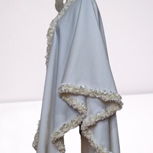 Side view of an off-white cashmere wedding cape showcasing the draped flow of the fabric and the textured handmade trim along the edges. Elegant, vintage-inspired bridal shawl displayed on a mannequin.