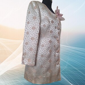 May include: A long-sleeved, cream-colored jacket with a floral pattern. The jacket has a button closure and a pink flower embellishment on the collar.