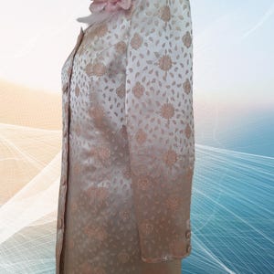 May include: A long-sleeved, cream-colored jacket with a floral pattern. The jacket has a pink flower with a white fur trim on the collar.