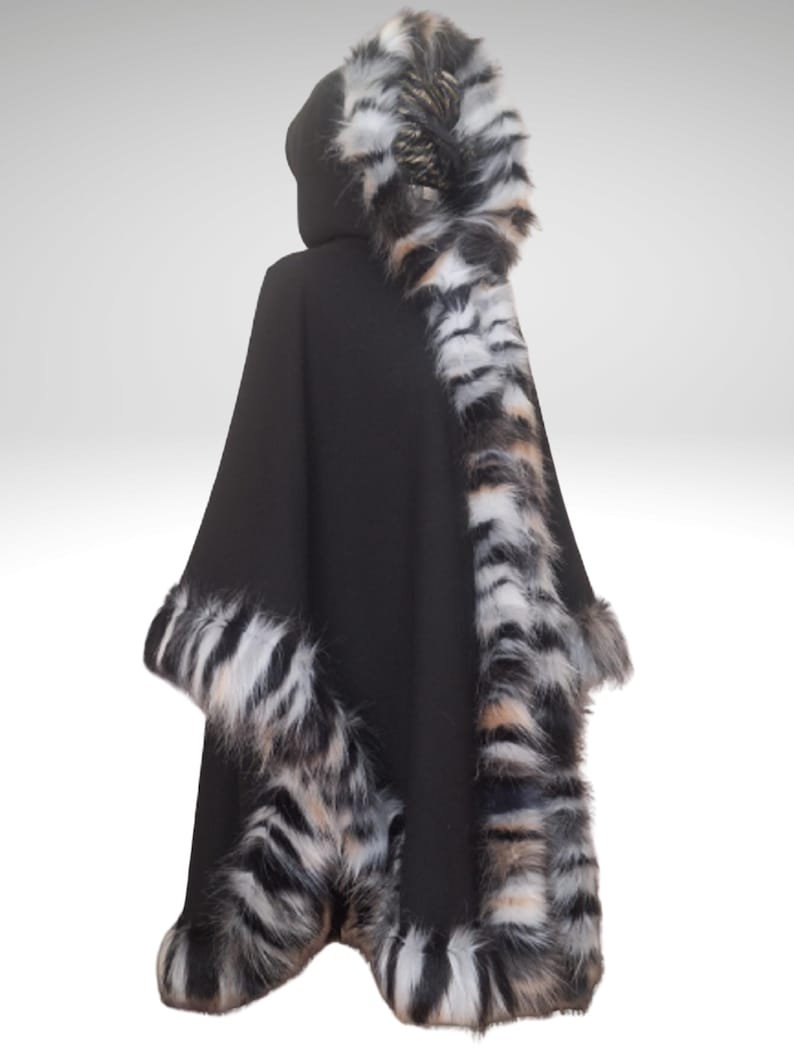 May include: Black hooded cape with faux fur trim. The cape features a hood and is trimmed with a striped pattern of black, white, and tan faux fur along the hood, sleeves, and hemline. The cape is made of a soft, dark fabric.