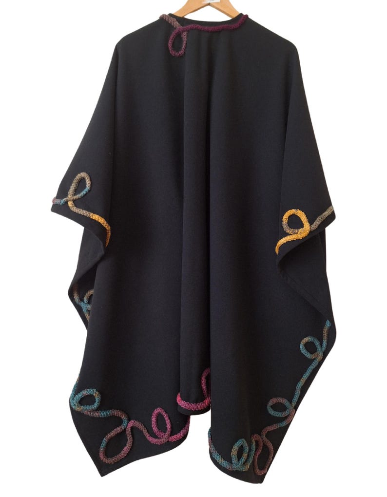 Luxurious cashmere wool cape handcrafted with artistic embellishments and an elegant draped silhouette. A timeless plus size statement piece for winter layering. The garment is shown on a hanger against a white background