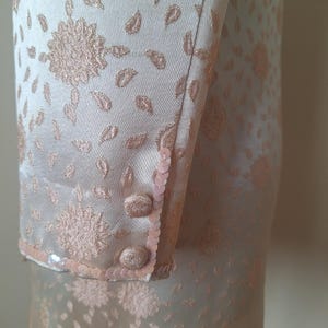 May include: A pale pink dress with a floral pattern and sequins on the cuffs. The dress is made of a silky fabric.
