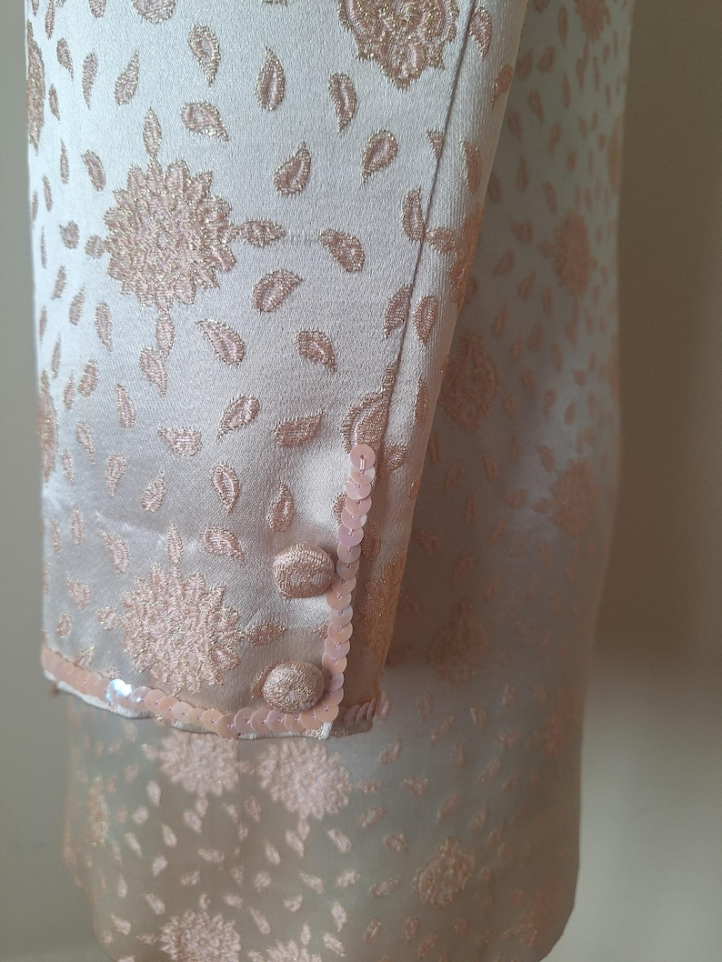 May include: A pale pink dress with a floral pattern and sequins on the cuffs. The dress is made of a silky fabric.