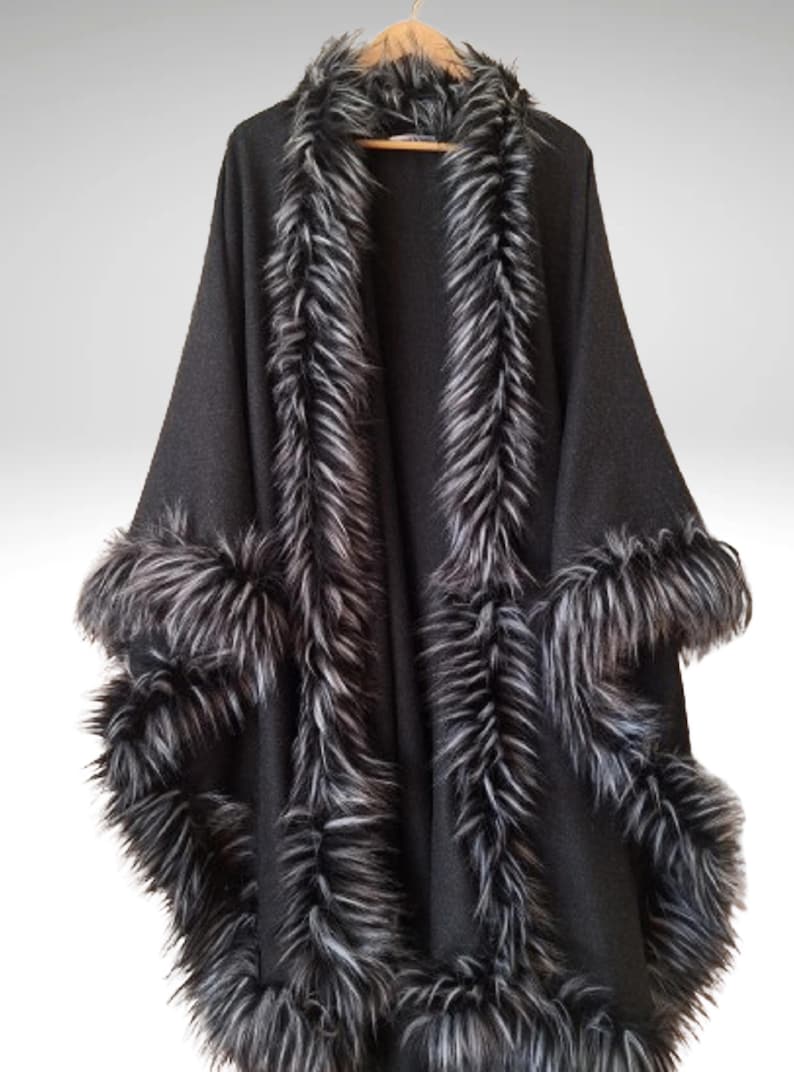 May include: A black cape with faux fur trim. The cape has a wide collar and trim along the edges and sleeves. The faux fur is a mix of black and grey, creating a striking contrast against the solid black fabric.