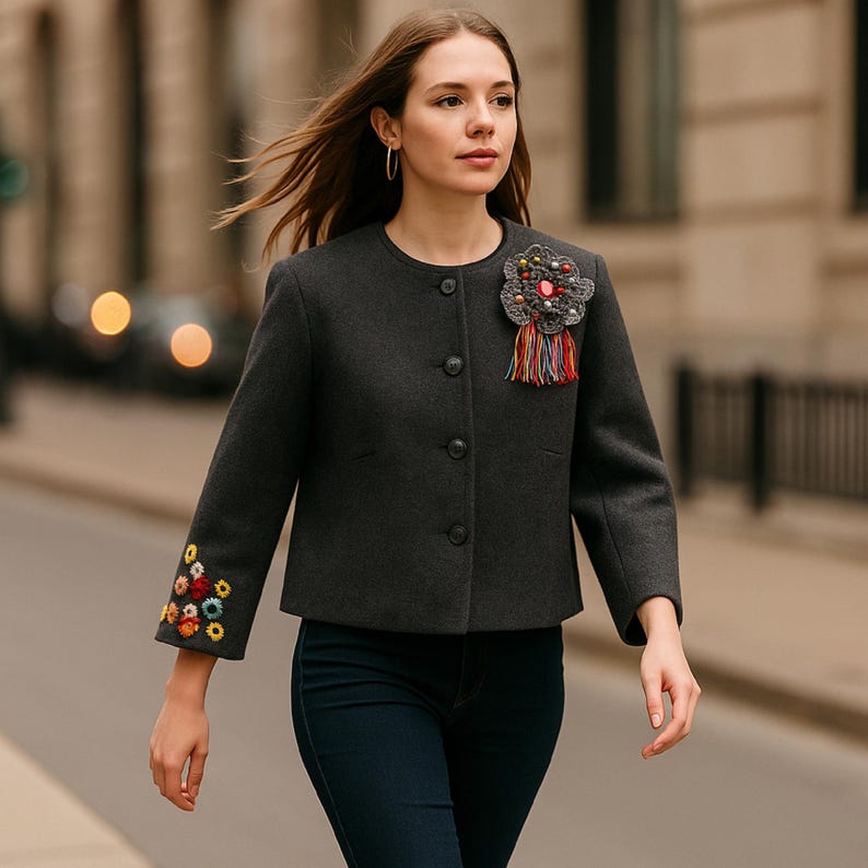 "Artisan handmade wool and alpaca cropped jacket, featuring vibrant hand-embroidered floral details on the sleeves and a unique handcrafted brooch – a one-of-a-kind design celebrating craftsmanship and color."