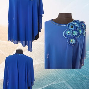 May include: A royal blue cape-style top with a round neckline and floral embellishments. The top features a flowing, asymmetrical design with layered sleeves. The neckline is adorned with sequins, and the shoulder has a cluster of fabric flowers.