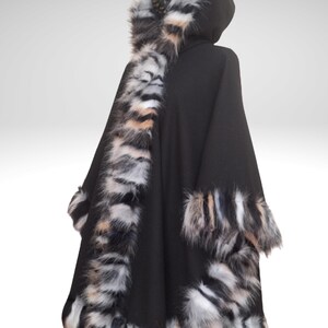 May include: A black hooded cape with faux fur trim. The cape features a hood and is trimmed with a mix of black, white, and tan faux fur along the edges and hood. The cape is designed to be worn over the shoulders.