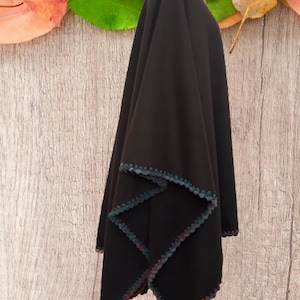 Side view ofReversible  brown poncho with a crocheted trim in shades of blue, green, and pink. The poncho is displayed on a mannequin against a woodgrain background.