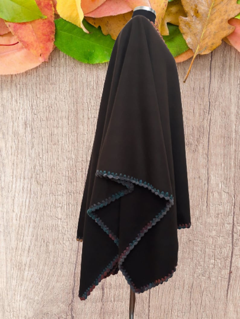Side view ofReversible  brown poncho with a crocheted trim in shades of blue, green, and pink. The poncho is displayed on a mannequin against a woodgrain background.