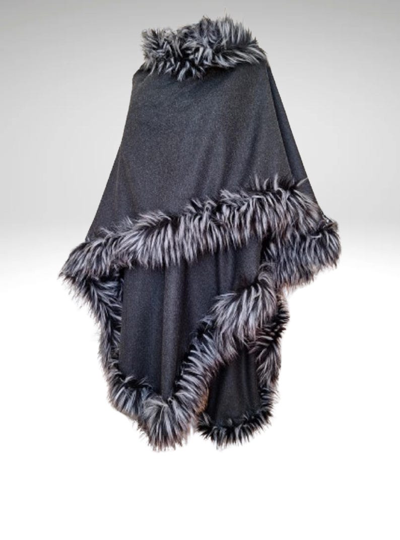 May include: A dark grey poncho with faux fur trim. The poncho has a faux fur collar and a border of black and white faux fur. The garment is displayed against a white background.