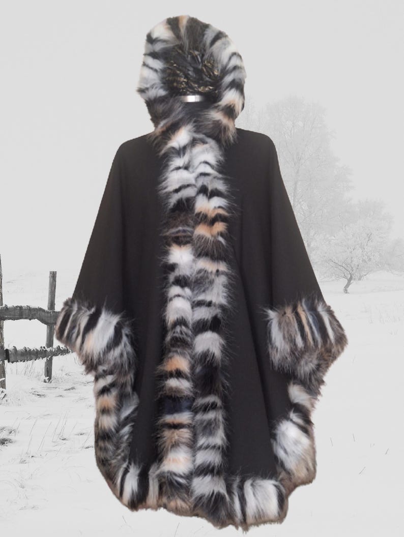 Front side view of black hooded cape featuring dense, long-pile  fur trim in black, white, and caramel hues — luxury handmade winter fashion