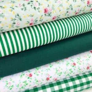 May include: A stack of four different green and white patterned fabrics. The top fabric has a small floral pattern, the second fabric has white stripes on a green background, the third fabric is solid green, and the bottom fabric has a green and white gingham pattern.