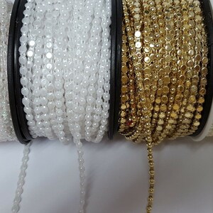 May include: Three spools of trim, one white, one gold, and one ivory. The trim is made of small round beads.