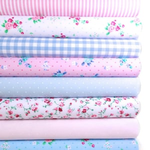 K&ouml;nnte beinhalten: Ein Stapel Stoffrollen in verschiedenen Mustern und Farben. Designs umfassen Blumen, Streifen, Punkte und Vichy in Rosa- und Blaut&ouml;nen. Die Stoffe sind eng gerollt und zeigen die Vielfalt der Texturen und Drucke.