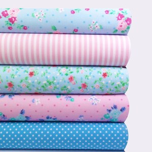 K&ouml;nnte beinhalten: Ein Stapel Stoffrollen mit verschiedenen Mustern. Die Muster umfassen Blumen, Streifen und Punkte in Blau-, Rosa- und Wei&szlig;t&ouml;nen. Der Stoff scheint Baumwolle oder ein &auml;hnliches Material zu sein, das sich zum Quilten oder Basteln eignet.