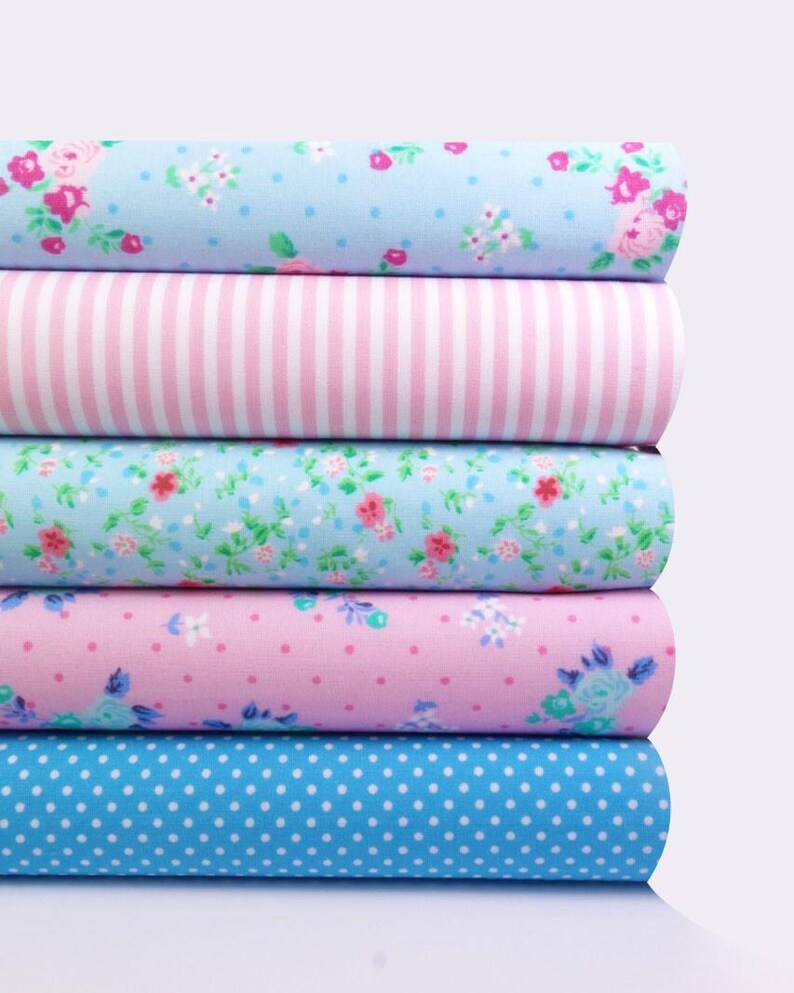 K&ouml;nnte beinhalten: Ein Stapel Stoffrollen mit verschiedenen Mustern. Die Muster umfassen Blumen, Streifen und Punkte in Blau-, Rosa- und Wei&szlig;t&ouml;nen. Der Stoff scheint Baumwolle oder ein &auml;hnliches Material zu sein, das sich zum Quilten oder Basteln eignet.