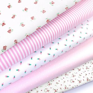 K&ouml;nnte beinhalten: Eine Auswahl an gerollten Stoffen mit verschiedenen Mustern. Die Stoffe umfassen Wei&szlig; mit rosa Streifen, Wei&szlig; mit kleinen rosa Blumen, einfarbiges Rosa, Wei&szlig; mit rosa Punkten und Wei&szlig; mit kleinen roten Blumen.
