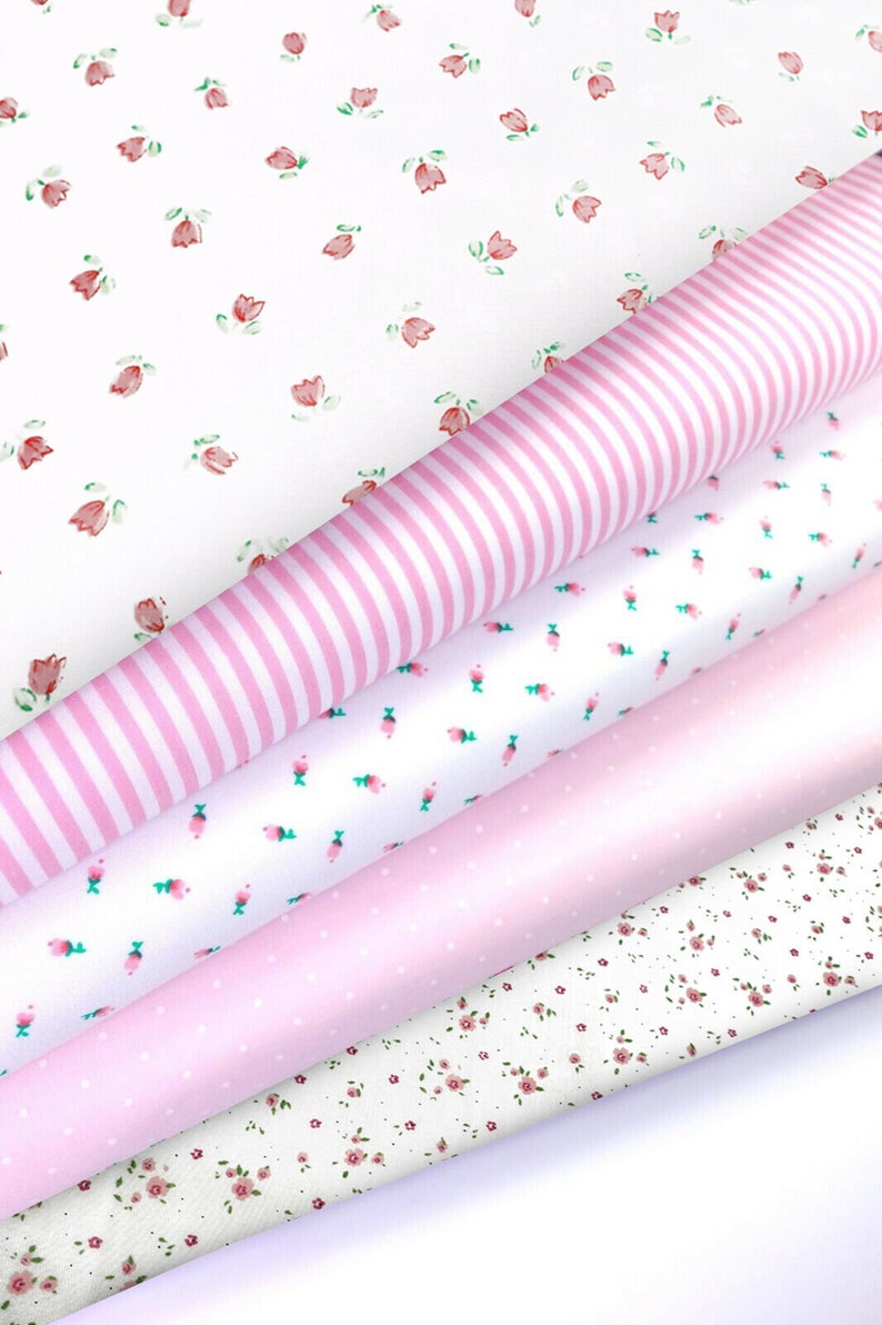 K&ouml;nnte beinhalten: Eine Auswahl an gerollten Stoffen mit verschiedenen Mustern. Die Stoffe umfassen Wei&szlig; mit rosa Streifen, Wei&szlig; mit kleinen rosa Blumen, einfarbiges Rosa, Wei&szlig; mit rosa Punkten und Wei&szlig; mit kleinen roten Blumen.