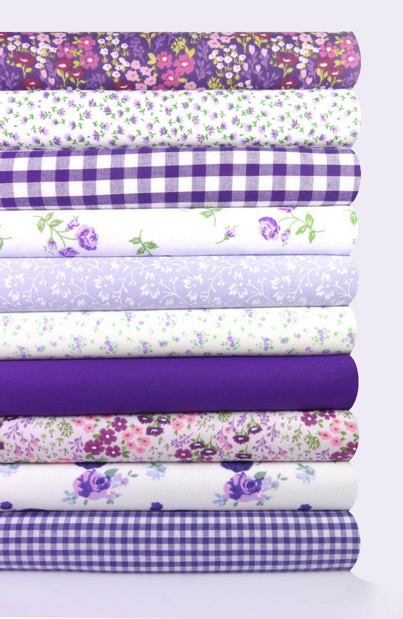 K&ouml;nnte beinhalten: Ein Stapel verschiedener lila Stoffrollen. Die Stoffe umfassen florale Muster, Vichy-Karos und unifarbene Stoffe. Die Farbpalette reicht von hellem Lavendel bis zu tiefem Violett und bietet eine Vielzahl von Texturen und Designs f&uuml;r N&auml;hprojekte.
