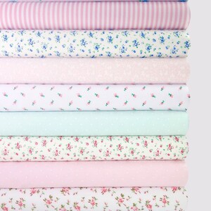 May include: A stack of 10 fabric rolls with various floral patterns in shades of pink, white, and light blue.
