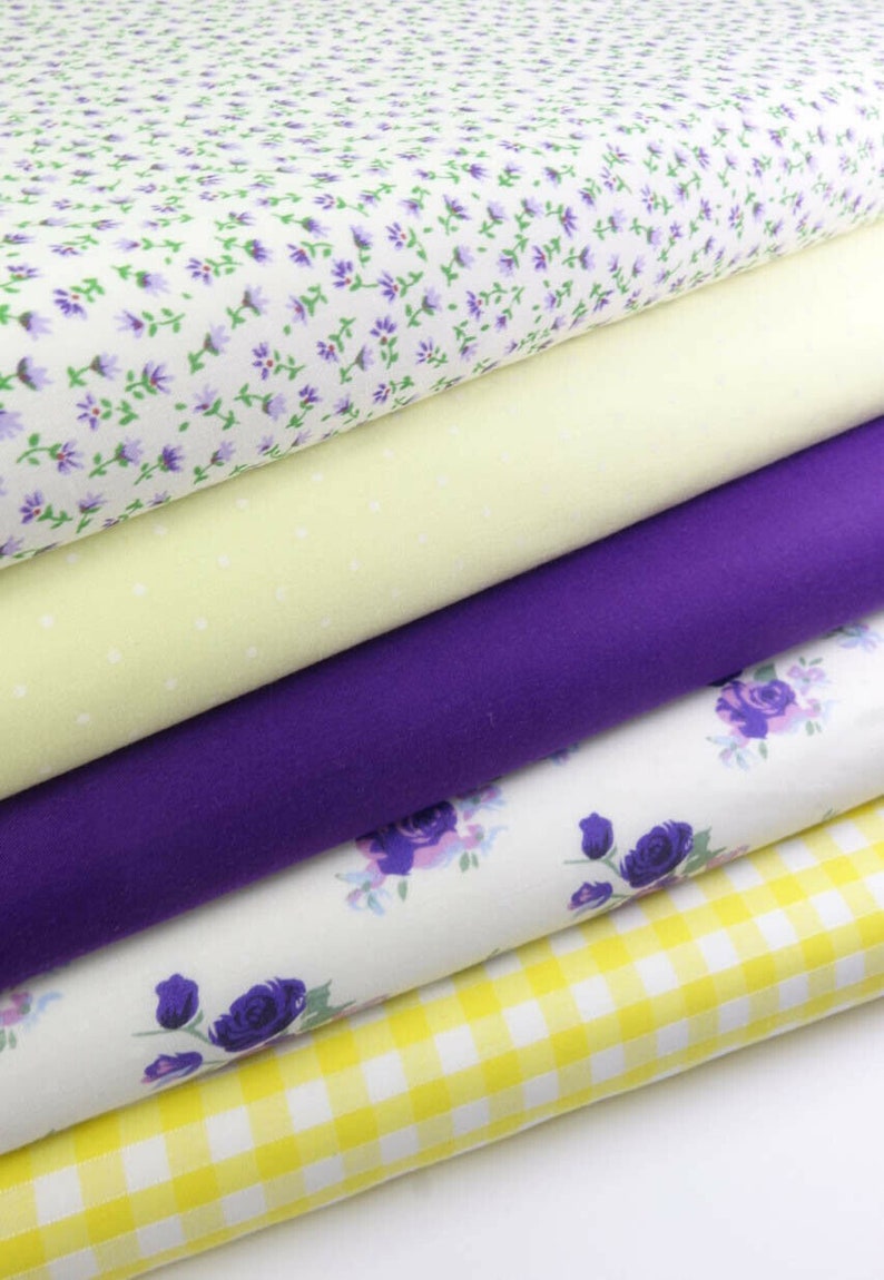 May include: A stack of five fabric swatches in various patterns and colors. The top swatch is white with a small purple floral print. The second swatch is a pale yellow with white polka dots. The third swatch is a solid purple. The fourth swatch is white with a larger purple floral print. The bottom swatch is a yellow and white gingham pattern.
