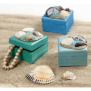 May include: Three small wooden boxes decorated with seashells and sand. The boxes are painted in shades of blue and green. One box has a pearl necklace inside.