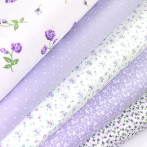 K&ouml;nnte beinhalten: Eine Auswahl an floralen Stoffrollen in Wei&szlig;- und Lavendelt&ouml;nen. Die Stoffe zeigen verschiedene Muster, darunter kleine lila Rosen, Tupfen und zarte Blumenranken. Ideal f&uuml;r Quilt- und Bastelprojekte.