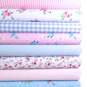 K&ouml;nnte beinhalten: Ein Stapel gerollter Stoffballen in verschiedenen Pastellfarben. Die Muster umfassen Blumenmuster, Streifen, Tupfen und Vichy-Karos. Die Farbpalette besteht aus Hellblau, Rosa und Wei&szlig; und erzeugt eine weiche, feminine &Auml;sthetik.