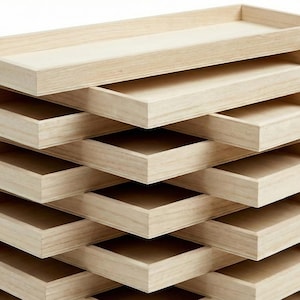 May include: A stack of light-coloured wooden trays, each with a rectangular shape and raised edges. The trays are arranged in a staggered, layered design, creating a visually interesting display. The wood grain is visible, adding to the natural aesthetic.