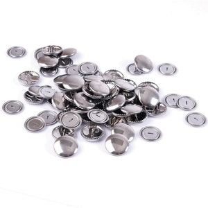 May include: A pile of silver metal buttons with a hole in the centre. The buttons are arranged in a random pattern on a white background.