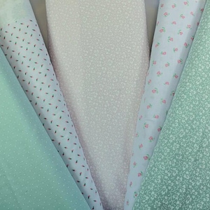 K&ouml;nnte beinhalten: Eine Auswahl an Stoffrollen in Pastellt&ouml;nen. Die Stoffe umfassen hellgr&uuml;n mit wei&szlig;en Punkten, Wei&szlig; mit winzigen roten und schwarzen Formen, blassrosa, hellblau mit kleinen rosa Blumen und hellgr&uuml;n mit winzigen wei&szlig;en Blumen.