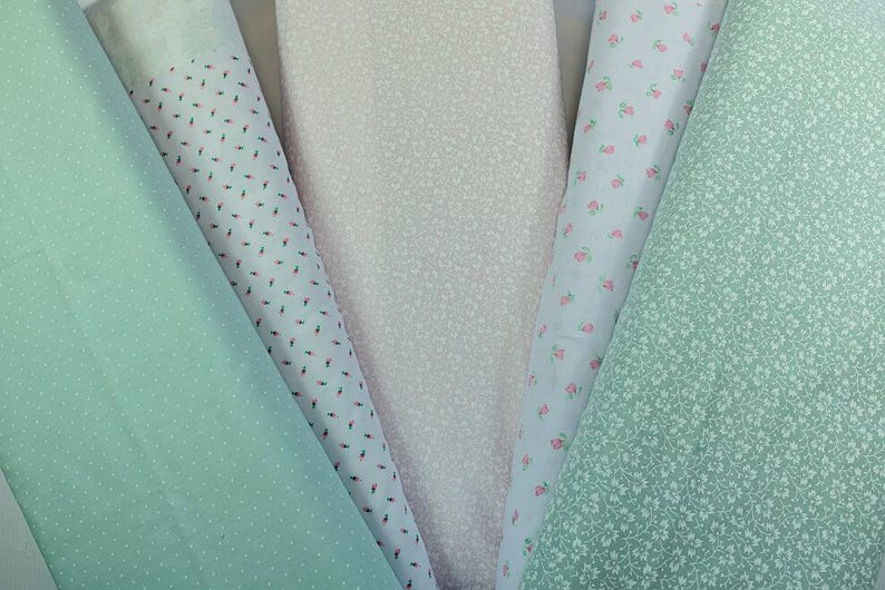 K&ouml;nnte beinhalten: Eine Auswahl an Stoffrollen in Pastellt&ouml;nen. Die Stoffe umfassen hellgr&uuml;n mit wei&szlig;en Punkten, Wei&szlig; mit winzigen roten und schwarzen Formen, blassrosa, hellblau mit kleinen rosa Blumen und hellgr&uuml;n mit winzigen wei&szlig;en Blumen.