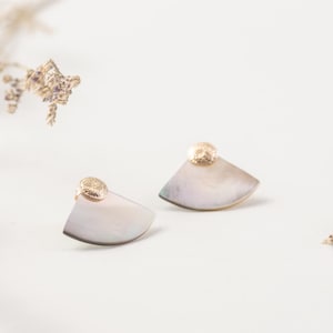 May include: A pair of earrings with a gold accent and a shell-shaped design. The earrings are a light gray color.