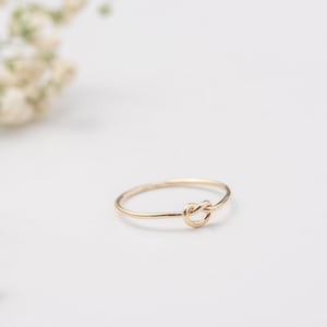 Puede incluir: Un anillo de oro simple con un diseño de nudo. El anillo es delicado y minimalista.