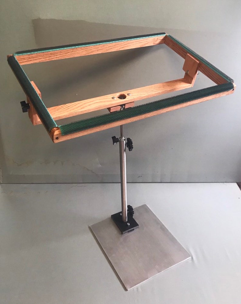 May include: A wooden embroidery hoop stand with a metal base and adjustable height. The hoop is made of natural wood with a green fabric lining.