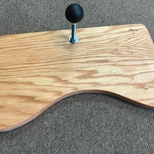 May include: A wooden base with a curved edge and a black knob on a silver shaft.